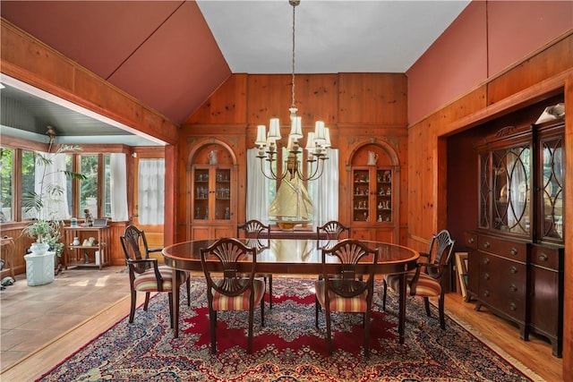 dining space featuring light hardwood / wood-style floors, lofted ceiling, wooden walls, and a chandelier