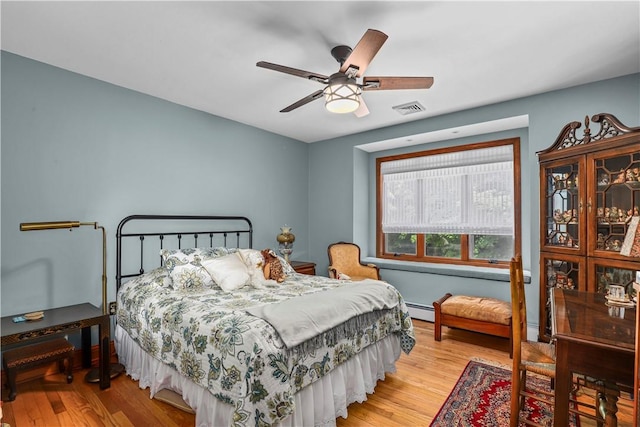 bedroom with ceiling fan, light hardwood / wood-style floors, and a baseboard heating unit