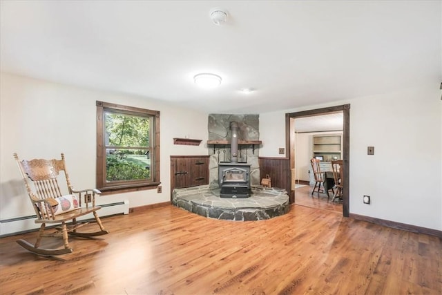 living area with baseboard heating, a wood stove, and hardwood / wood-style flooring