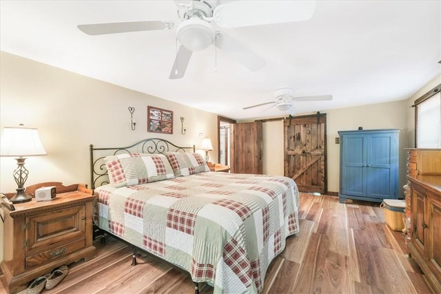 bedroom featuring wood-type flooring, a barn door, and ceiling fan