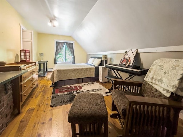 bedroom with a baseboard heating unit, vaulted ceiling, and light wood-type flooring