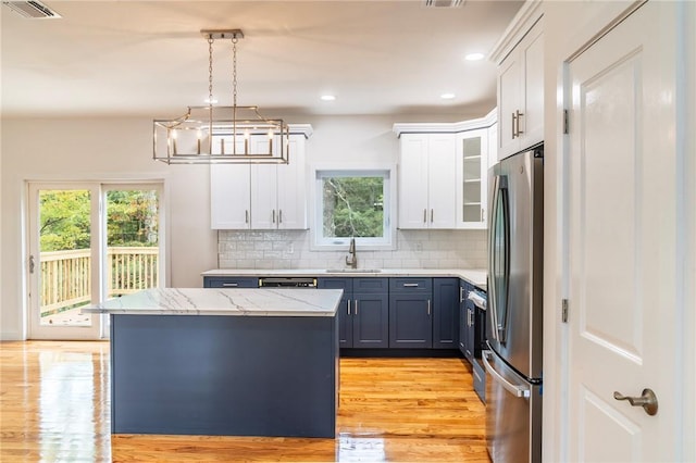 kitchen featuring pendant lighting, white cabinets, sink, light hardwood / wood-style flooring, and stainless steel fridge