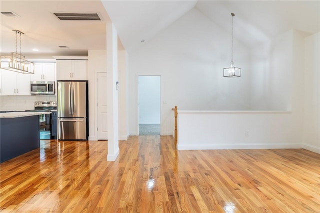 kitchen featuring white cabinets, light wood-type flooring, hanging light fixtures, and appliances with stainless steel finishes