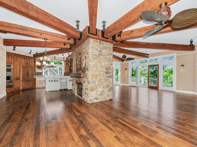 unfurnished living room with vaulted ceiling with beams, dark hardwood / wood-style floors, a stone fireplace, and ceiling fan