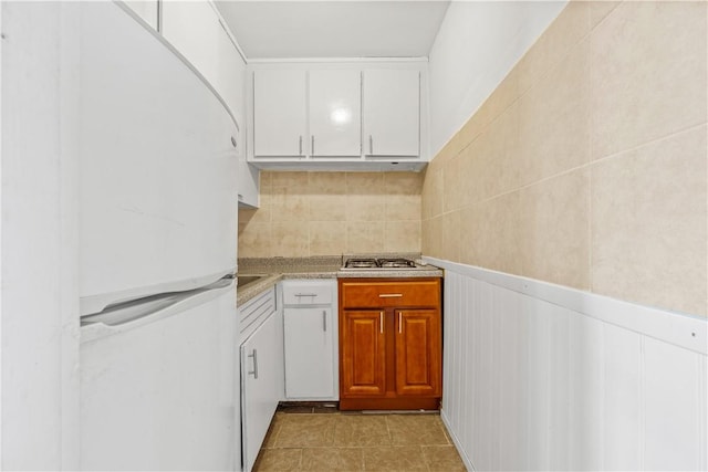 kitchen featuring white cabinets, white fridge, light tile patterned flooring, and stainless steel gas cooktop