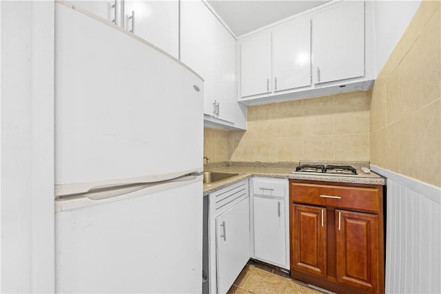 kitchen featuring white cabinetry, gas stovetop, tasteful backsplash, white refrigerator, and light tile patterned flooring