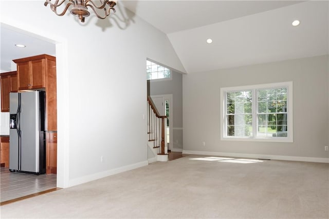 unfurnished living room with light carpet, lofted ceiling, and a notable chandelier