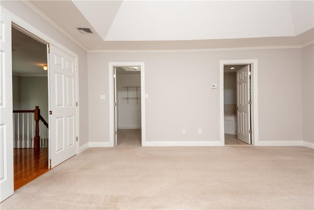 unfurnished bedroom with a walk in closet, crown molding, ensuite bath, light colored carpet, and a closet