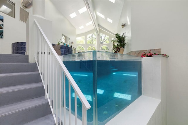 staircase with beam ceiling, high vaulted ceiling, a skylight, and track lighting