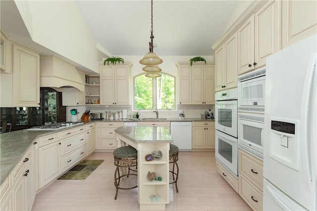 kitchen with sink, cream cabinetry, decorative light fixtures, white appliances, and a breakfast bar