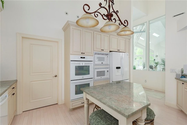 kitchen featuring light stone countertops, white appliances, decorative light fixtures, cream cabinetry, and a breakfast bar area