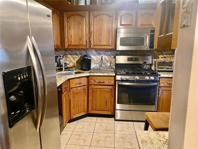 kitchen with light stone countertops, backsplash, stainless steel appliances, sink, and light tile patterned flooring