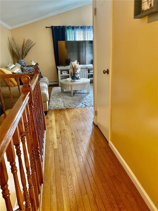 corridor featuring hardwood / wood-style floors, vaulted ceiling, baseboard heating, and crown molding