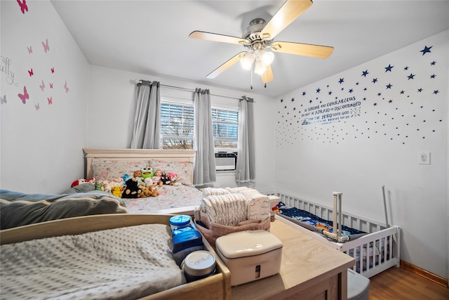 bedroom featuring ceiling fan, hardwood / wood-style floors, and a crib