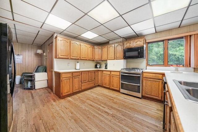 kitchen featuring light hardwood / wood-style flooring, a drop ceiling, wood walls, and black appliances