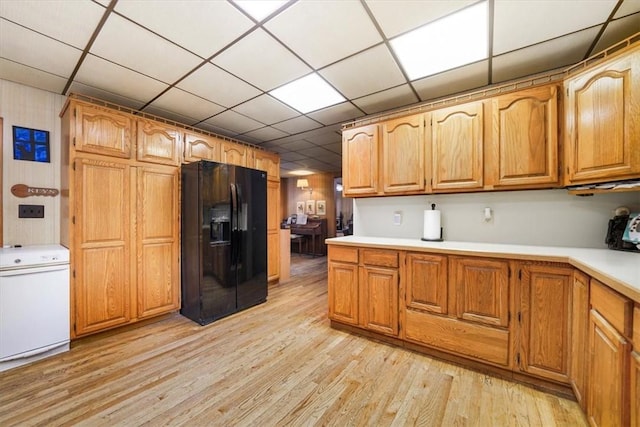 kitchen featuring a drop ceiling, black fridge, and light wood-type flooring