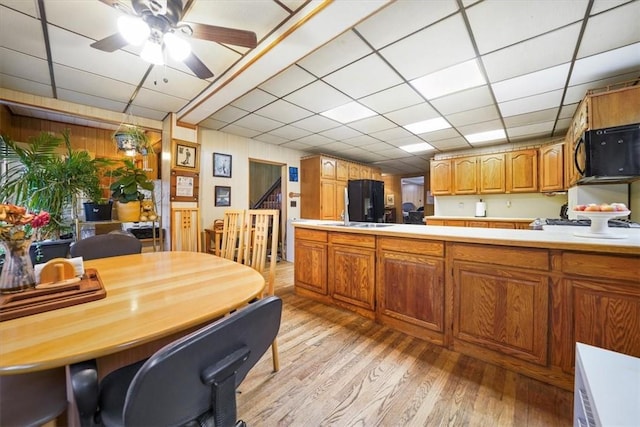 kitchen featuring a paneled ceiling, wood walls, black appliances, ceiling fan, and light hardwood / wood-style floors