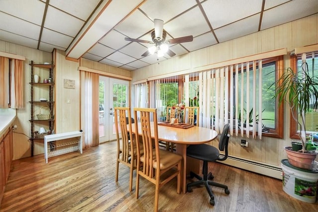 dining area featuring ceiling fan, a drop ceiling, a baseboard radiator, wood walls, and hardwood / wood-style floors