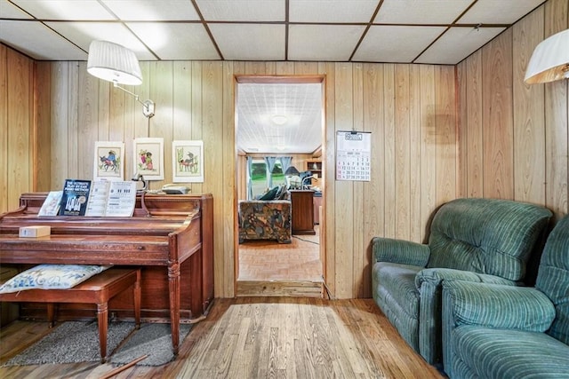 living area featuring wooden walls, a drop ceiling, and wood-type flooring