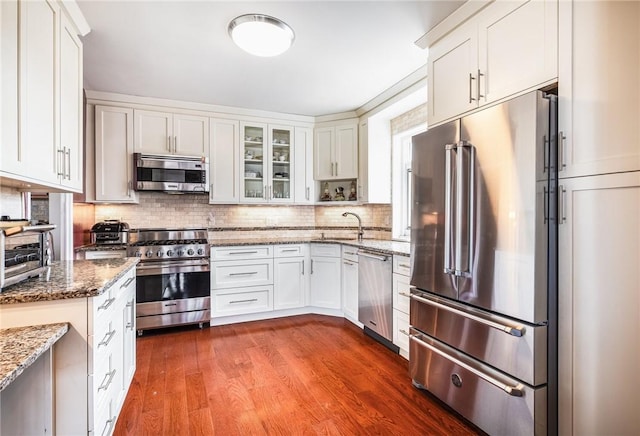 kitchen featuring hardwood / wood-style floors, premium appliances, white cabinetry, and stone counters