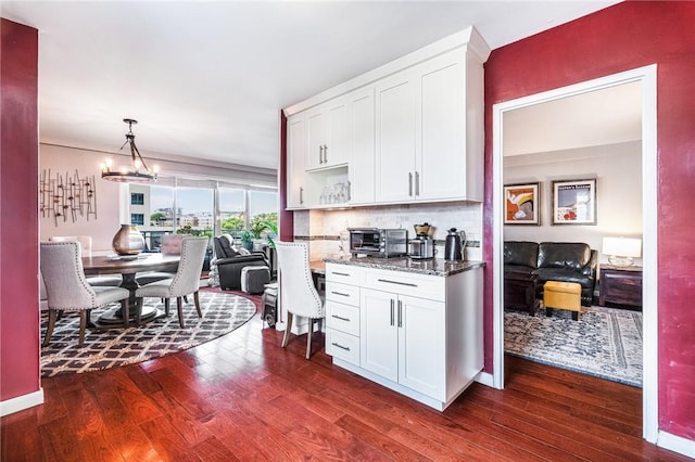 kitchen featuring pendant lighting, dark wood-type flooring, stone counters, white cabinets, and decorative backsplash