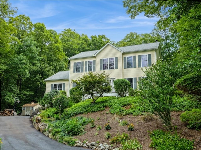 colonial inspired home with driveway, a shed, and an outbuilding