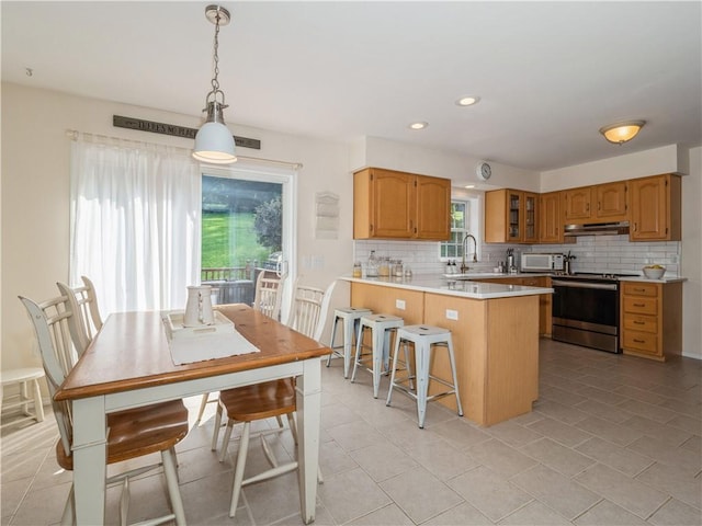 kitchen with brown cabinetry, electric stove, glass insert cabinets, hanging light fixtures, and light countertops