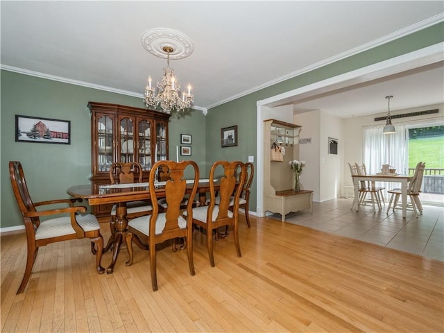 dining room with ornamental molding, light wood-style flooring, baseboards, and an inviting chandelier