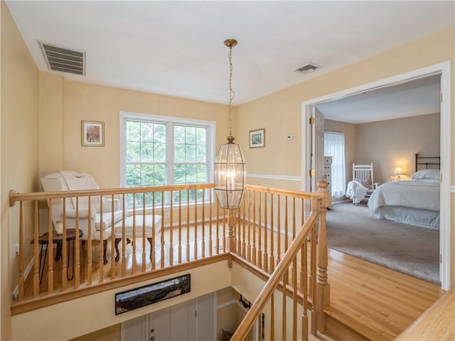 hallway featuring wood finished floors, an upstairs landing, visible vents, and a notable chandelier