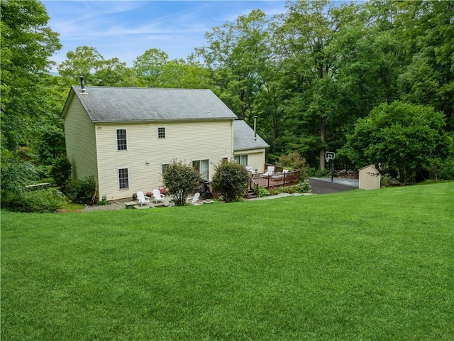 back of property with roof with shingles, a yard, a deck, and a storage unit