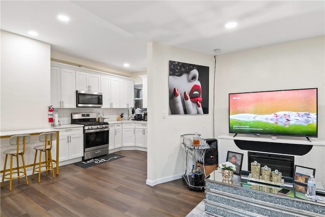 kitchen with appliances with stainless steel finishes, dark hardwood / wood-style flooring, tasteful backsplash, a fireplace, and white cabinets