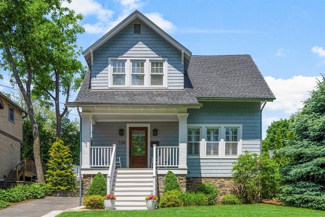 shingle-style home featuring covered porch, a shingled roof, and stairway