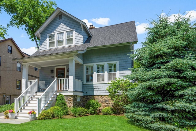 view of front of property featuring covered porch, roof with shingles, stairway, a chimney, and a front yard