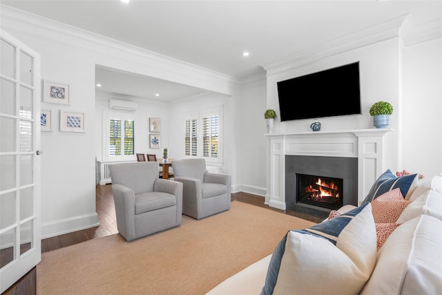 living room featuring baseboards, a wall unit AC, a fireplace with flush hearth, wood finished floors, and crown molding