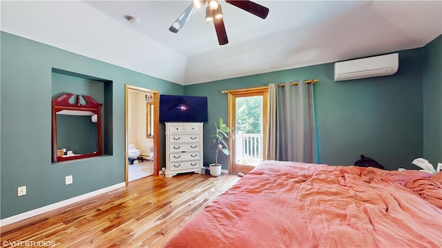 bedroom with connected bathroom, ceiling fan, a wall unit AC, hardwood / wood-style floors, and vaulted ceiling