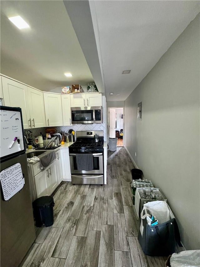 kitchen with white cabinets, appliances with stainless steel finishes, decorative backsplash, and light hardwood / wood-style flooring