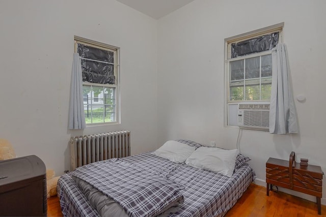 bedroom with radiator heating unit, cooling unit, and hardwood / wood-style flooring