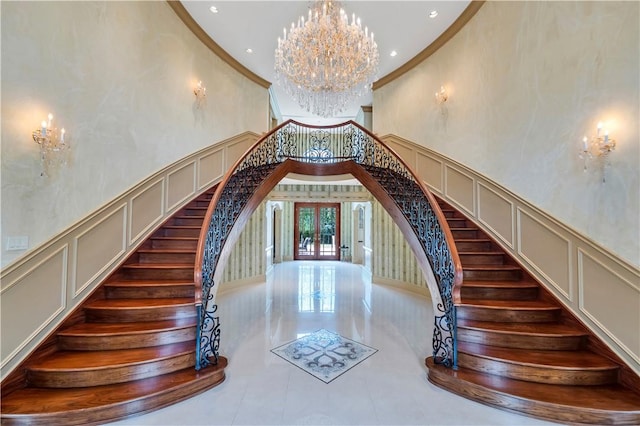 staircase featuring french doors, a towering ceiling, crown molding, and a notable chandelier