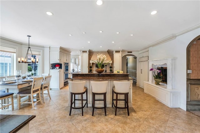 kitchen featuring a center island, an inviting chandelier, ornamental molding, decorative light fixtures, and a breakfast bar area