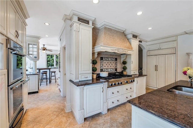 kitchen with sink, appliances with stainless steel finishes, white cabinets, custom range hood, and ornamental molding