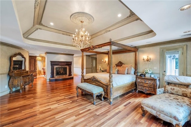 bedroom with a raised ceiling, a chandelier, ornamental molding, and light wood-type flooring