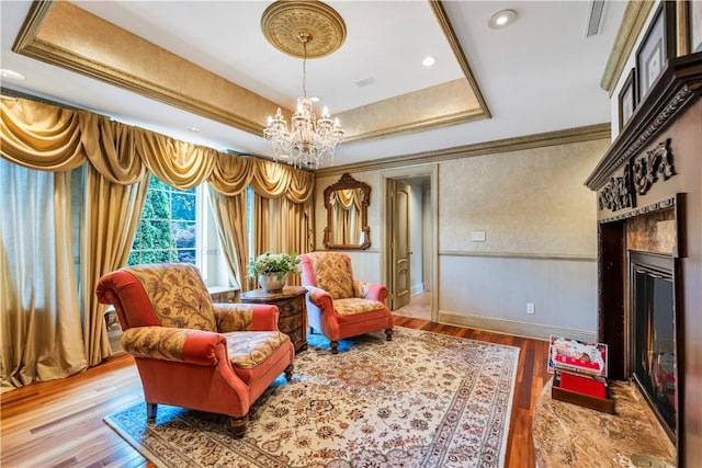 living area featuring ornamental molding, light hardwood / wood-style floors, an inviting chandelier, and a tray ceiling