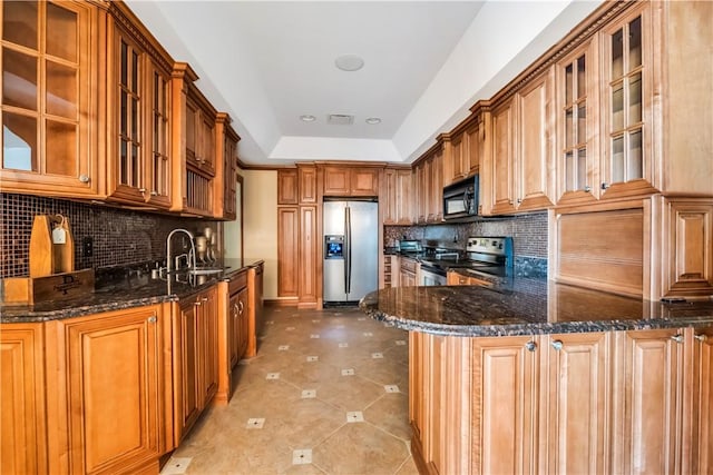 kitchen featuring sink, backsplash, kitchen peninsula, dark stone counters, and appliances with stainless steel finishes