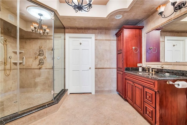 bathroom with vanity, a shower with door, tile walls, and an inviting chandelier