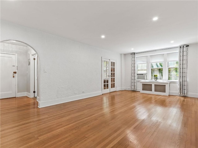 unfurnished living room featuring cooling unit, light hardwood / wood-style floors, radiator heating unit, and french doors