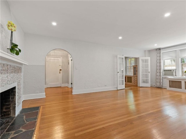 unfurnished living room featuring french doors, light hardwood / wood-style flooring, cooling unit, and a stone fireplace