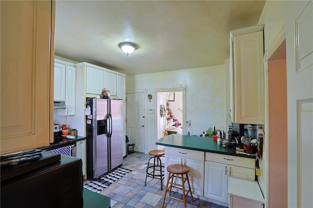 kitchen with a kitchen breakfast bar, stainless steel fridge, and white cabinets