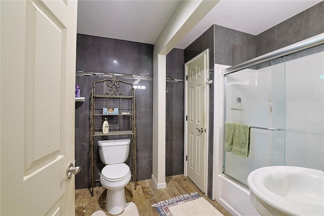 bathroom featuring toilet, tile walls, and combined bath / shower with glass door