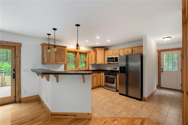 kitchen with kitchen peninsula, appliances with stainless steel finishes, plenty of natural light, and hanging light fixtures