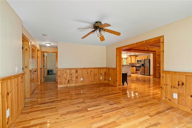 empty room with ceiling fan, wood walls, and light wood-type flooring